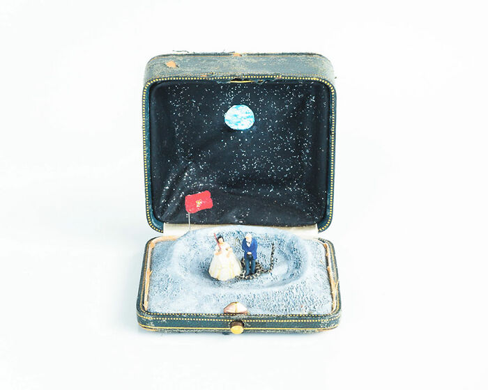Miniature scene in a box depicting a wedding on the moon with tiny figures, a flag, and Earth in the background.