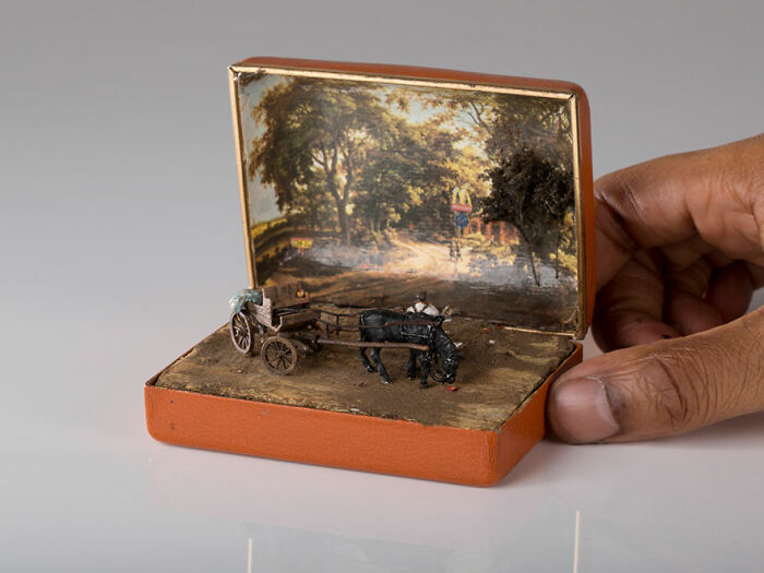 Hand holding a miniature scene with a horse and cart in a tiny box, representing secret worlds.