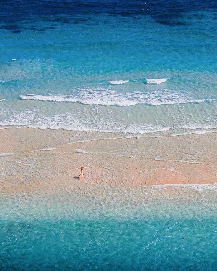 Aerial view of a person walking on a sandy beach surrounded by turquoise waters.