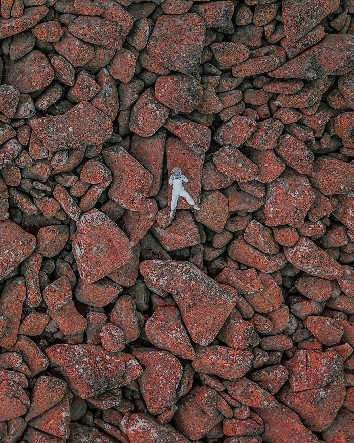 Drone photograph of a person in a white suit lying on red rocks, creating an intriguing contrast in texture.