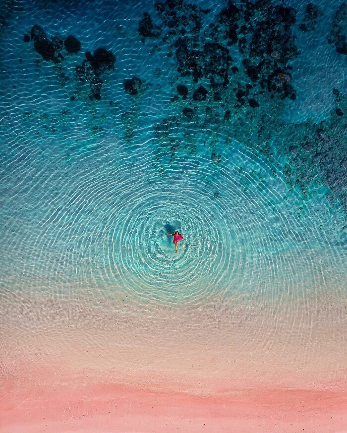 Drone photograph by Dimitar Karanikolov of a person in pink floating in clear blue water with ripples.