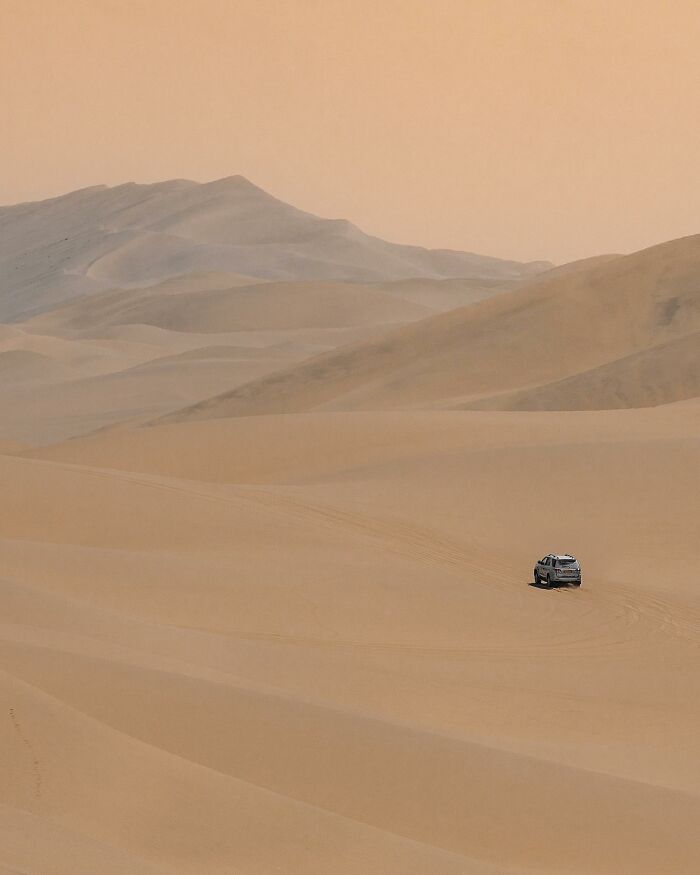 A captivating drone photograph of a solitary vehicle traversing vast desert dunes under a hazy sky.