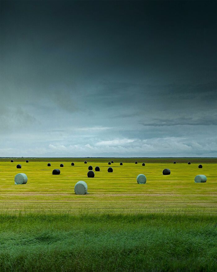 Drone photograph of a serene landscape with scattered hay bales under a moody sky.
