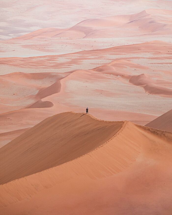 Aerial view of a solitary figure standing atop a vast desert dune, showcasing captivating drone photography.