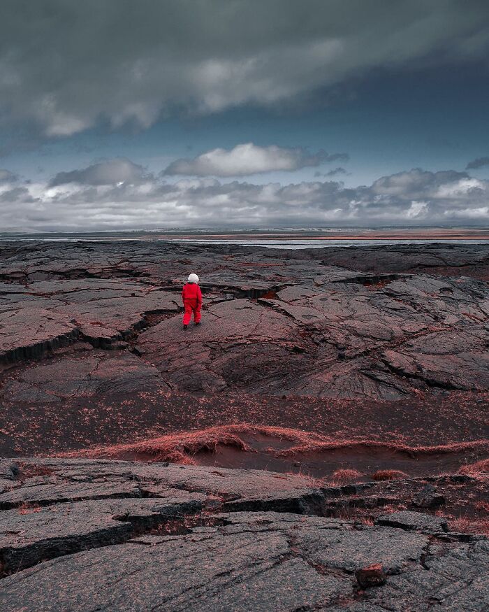 Person in red against a rocky, desolate landscape captured in a captivating drone photograph by Dimitar Karanikolov.