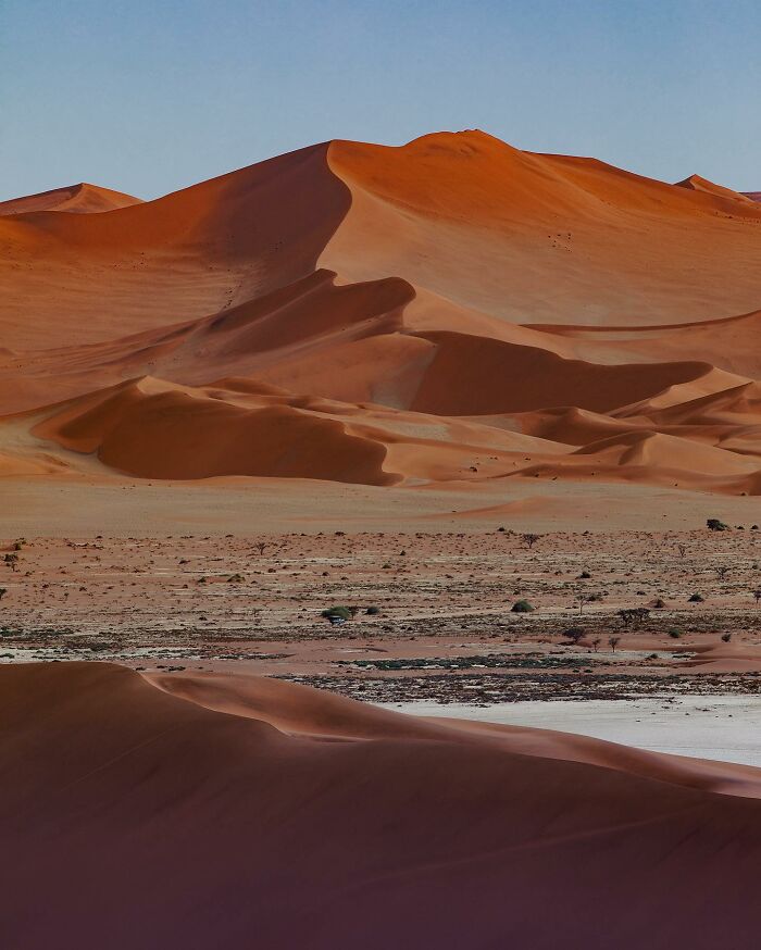 Drone photograph of sweeping red sand dunes against a clear blue sky.
