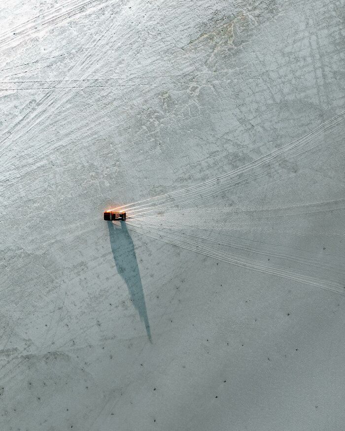 Aerial view of a lone vehicle on a snowy landscape, creating tracks, captured by drone photographer Dimitar Karanikolov.