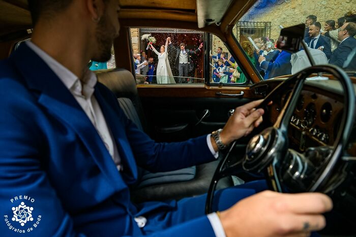 A bride and groom celebrate outside a vintage car while a driver in a blue suit looks on at the 2025 Premios FDB Awards.