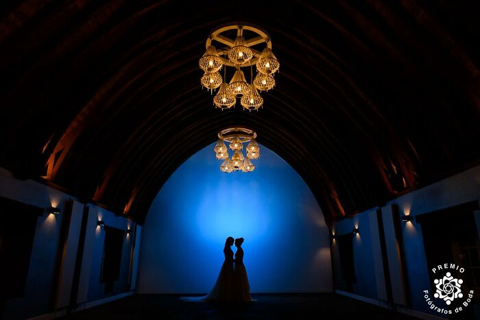 Silhouetted couple in elegant venue with chandeliers, featured in top wedding photos of 2025 Premios FDB Awards.