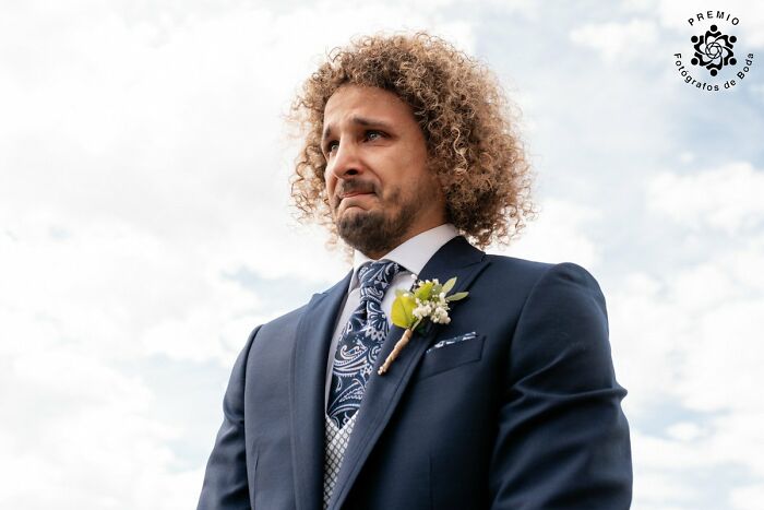 Man in a suit with a boutonnière at the 2025 Premios FDB Awards, looking emotional against a cloudy sky.