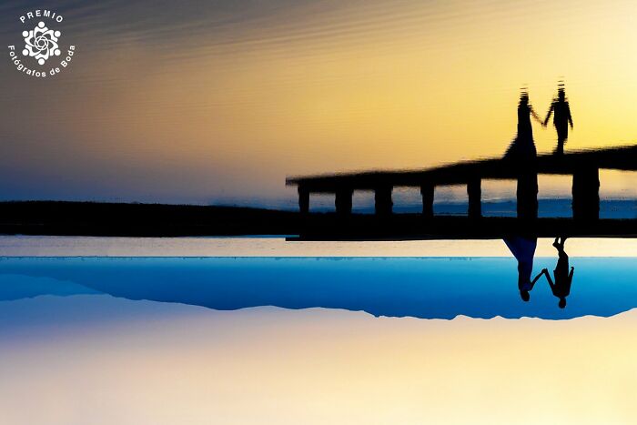 Silhouette of a couple on a pier with a sunset reflection, featured in Premios FDB wedding photo awards.