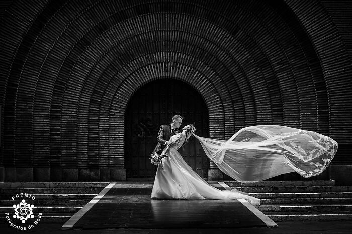 A couple poses dramatically in front of an archway, her veil flowing, at the 2025 Premios FDB wedding awards.