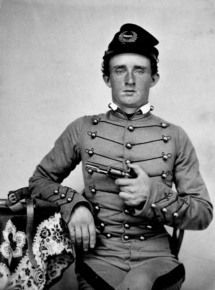 Young historical figure in vintage military uniform holding a pistol, posing for a rare black and white portrait photo.