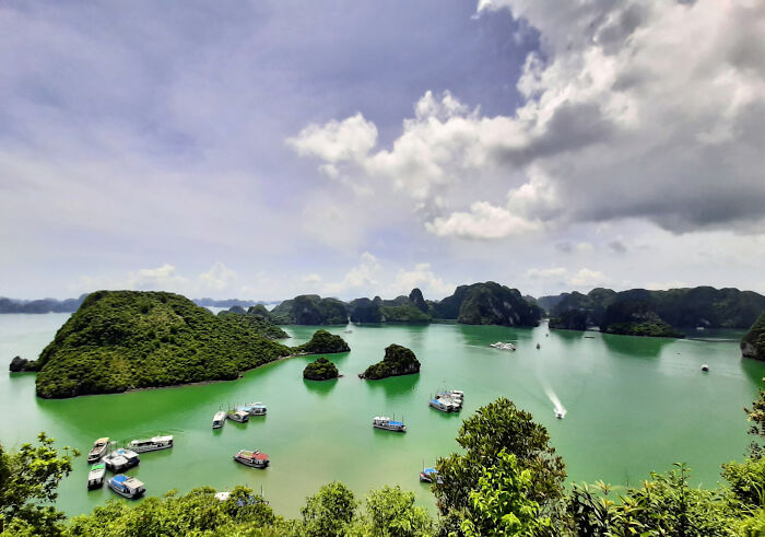 Stunning coastal vista with green islands, turquoise waters, and boats under a partly cloudy sky.