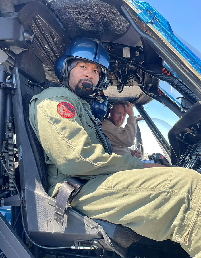 Former Navy SEAL in helicopter cockpit, wearing a helmet, with co-pilot in background.