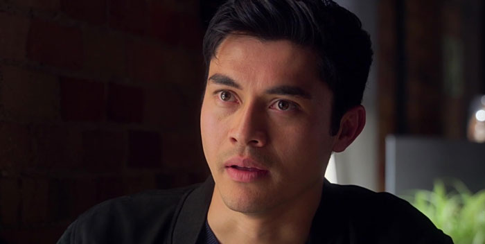 A man with short black hair in a thoughtful expression, sitting indoors.