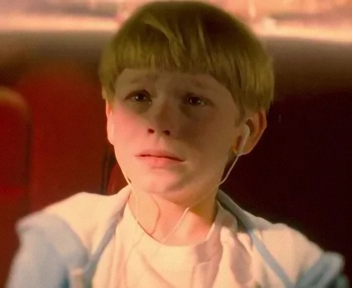 Young child actor with earphones, illuminated by soft light, looking solemn.