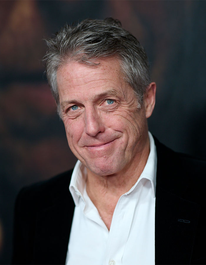 Hugh Grant at event, smiling in a white shirt and black jacket, discusses 'pathetic' school rules. Hugh Grant at event, smiling in a white shirt and black jacket, discusses 'pathetic' school rules.