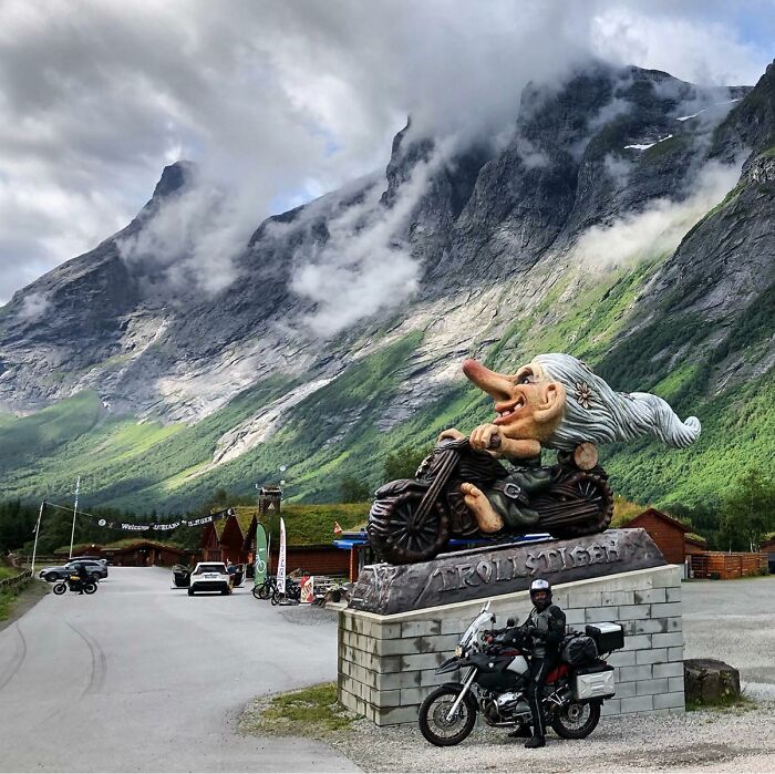 Whimsical outdoor troll sculpture on motorbike with mountains in the background.