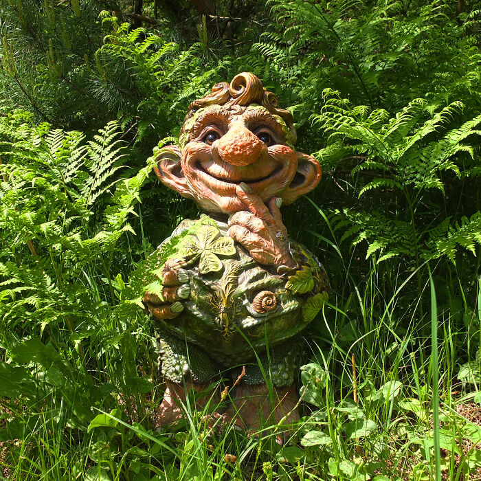 Whimsical troll sculpture made from outdoor materials, surrounded by lush greenery.