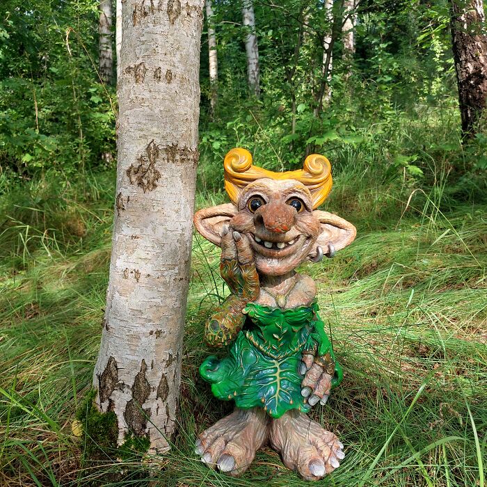 Whimsical troll sculpture crafted from outdoor materials, positioned beside a tree in a lush forest setting.