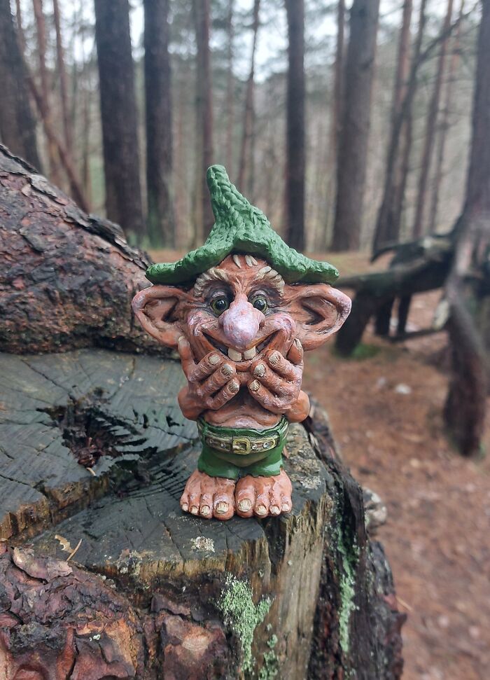 Whimsical troll sculpture on a tree stump in the forest, crafted from outdoor materials.