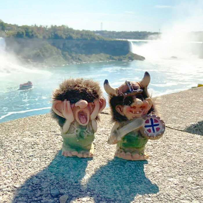 Whimsical trolls made from outdoor materials overlooking a waterfall, with one troll holding a small shield and helmet.