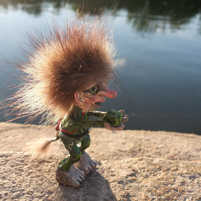 Whimsical troll sculpture made from outdoor materials, placed beside water on a sunny day.