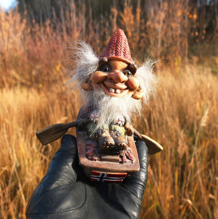 Whimsical troll figurine in a gloved hand, set against an autumnal outdoor backdrop.