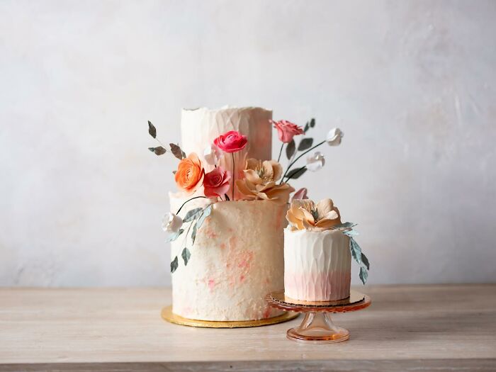 Visually stunning cakes with floral decorations on a wooden table, featuring intricate design and vegan ingredients.