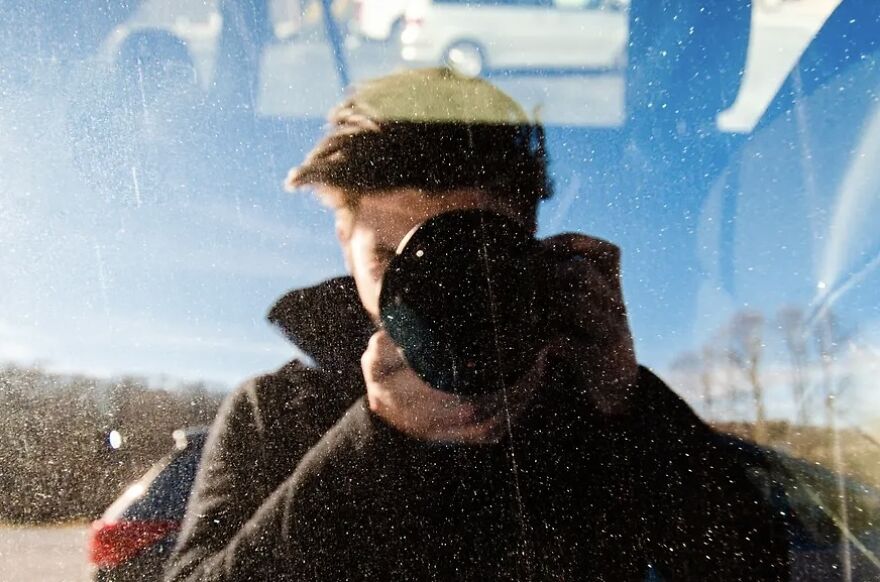 Person wearing a hat taking a photo reflected in a dusty window exploring the dominant trait concept through self-reflection.