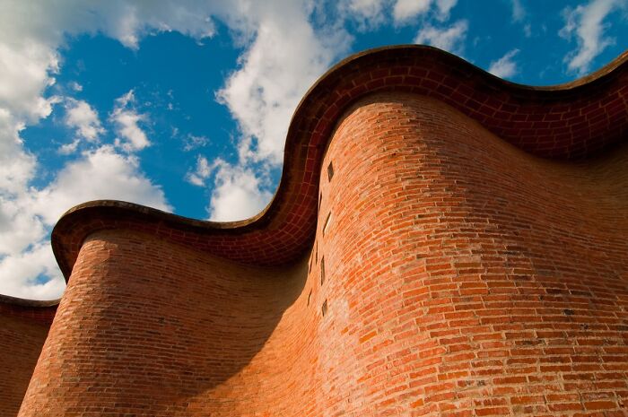 Curved brick structure against a blue sky, showcasing an architectural wonder not widely known.