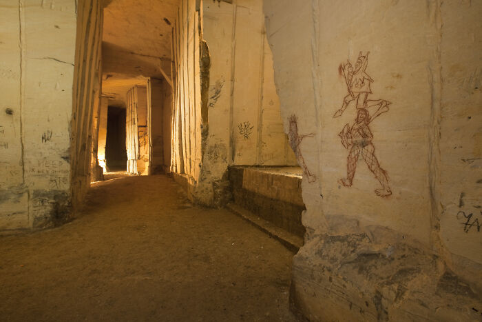 Ancient underground city corridor with stone walls featuring eerie drawings.