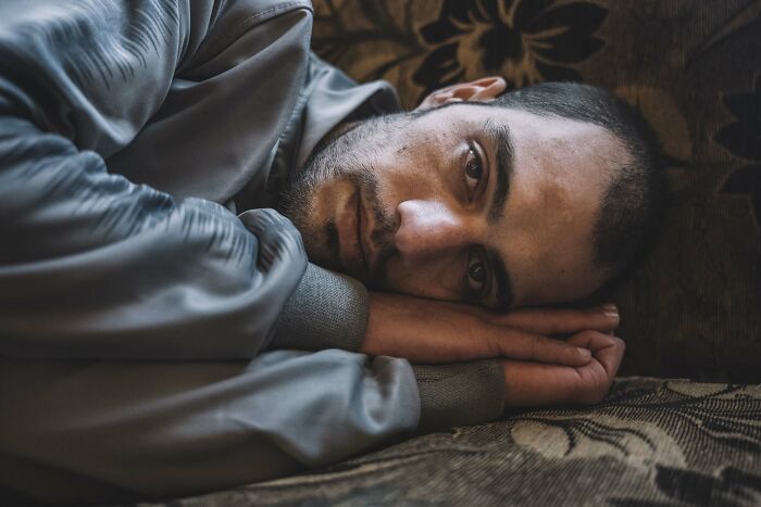 Man lying down, looking intently, wearing a grey jacket. Istanbul Photo Awards winning image 2025.