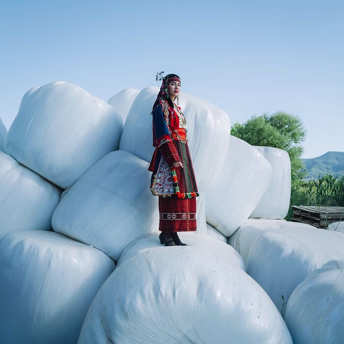 Woman in traditional dress standing on stacked white bales, Istanbul Photo Awards 2025.