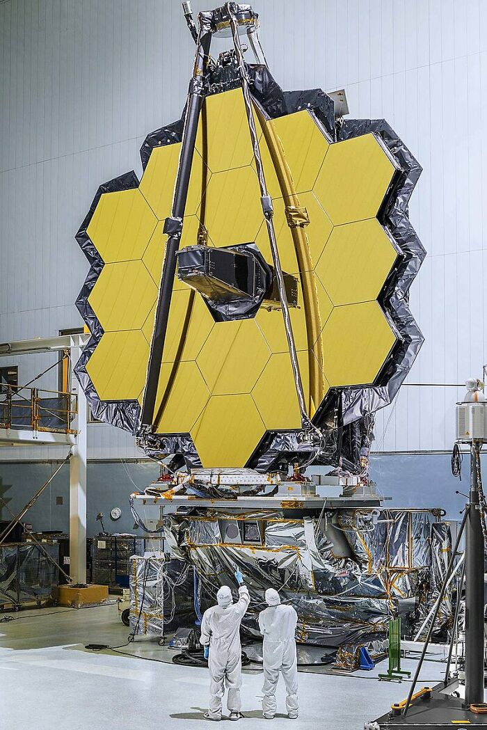 Scientists inspect a large space telescope, showcasing a peak moment in science's achievements.