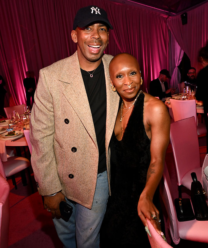 Two people smiling at a red carpet event, wearing stylish attire, highlighting behind-the-scenes realities.