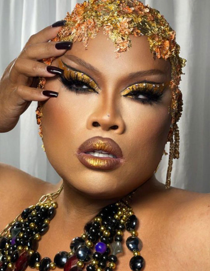Glamorous drag queen with stunning makeup, adorned in gold and black accessories.