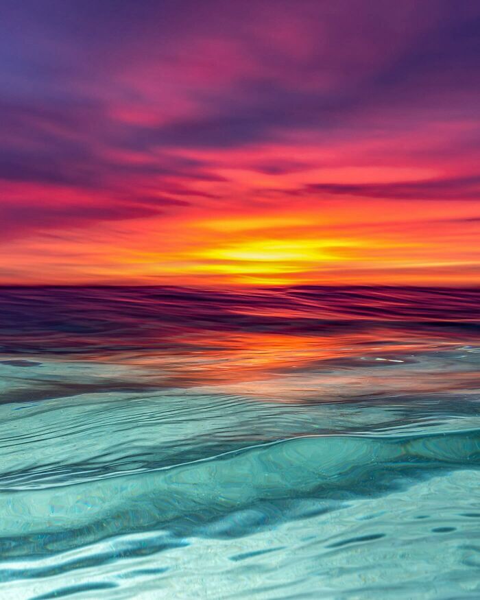 Ocean meets sky at sunset with vivid purple, pink, and orange hues reflecting on the water, captured in a stunning photo.