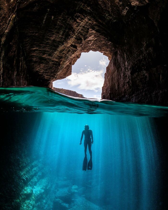 Silhouette of a diver ascending towards sunlight in an underwater cave, illustrating the ocean-meets-sky world.
