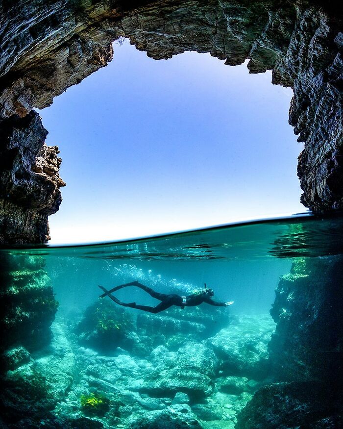 Diver explores underwater cave where ocean meets sky, captured by Jordan Robins.