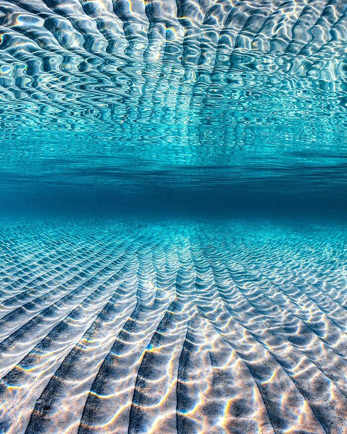 Ocean meets sky in a magical underwater scene with rippled sand and blue water, captured by Jordan Robins.