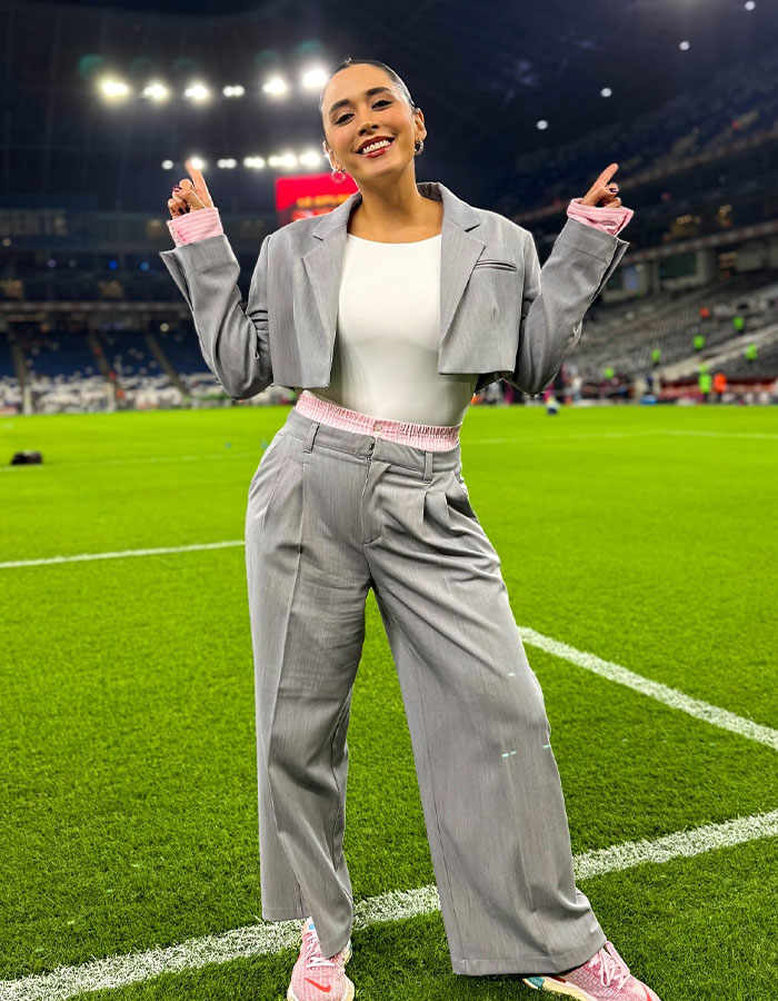 A female reporter in a grey suit smiles on a soccer field, highlighting media controversy over public reactions.