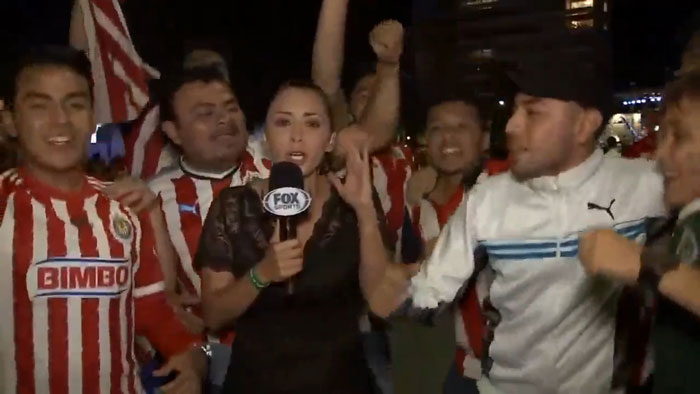 Female reporter surrounded by soccer fans on live TV.