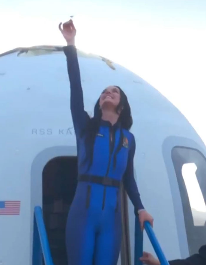 Person in space suit exits spacecraft, raising hand skyward, after a brief space trip.
