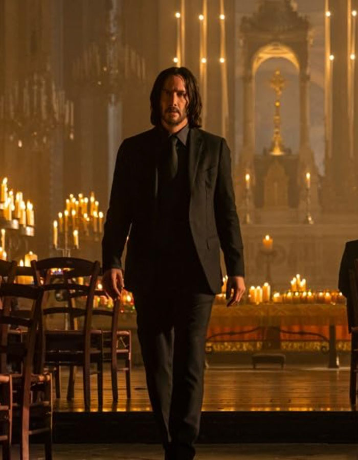 Keanu Reeves in a dimly lit setting, wearing a black suit, highlighting his youthful look.