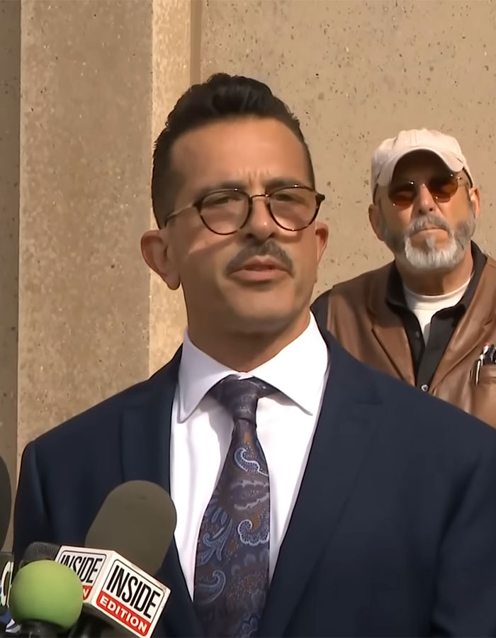 Man in a suit speaks at a press event, addressing a case about a woman who locked up her stepson for 20 years.
