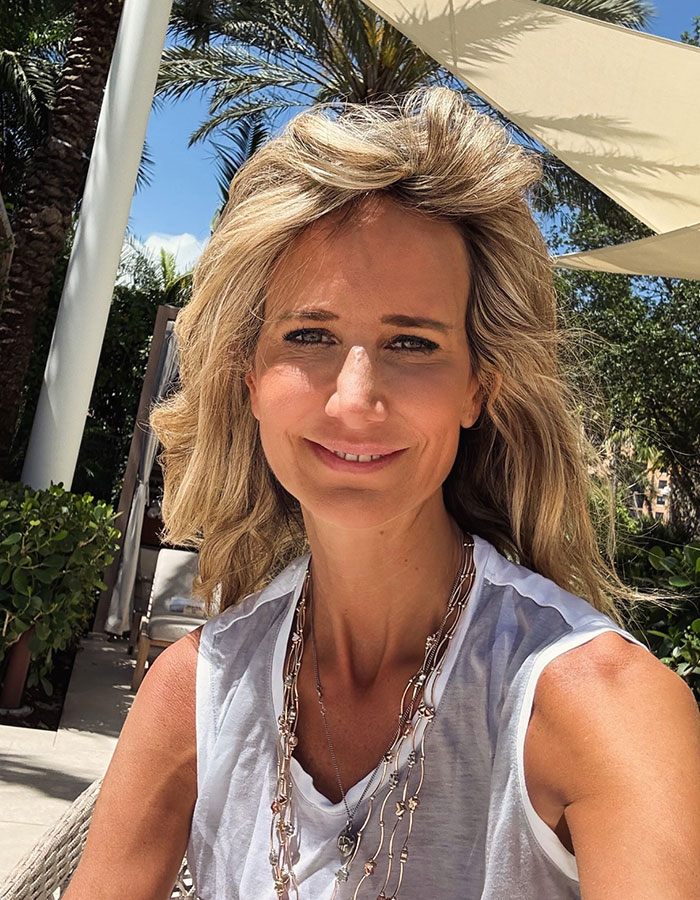 Woman in a white sleeveless top and necklace, smiling outdoors under a sunshade, relevant to Prince Andrew news.