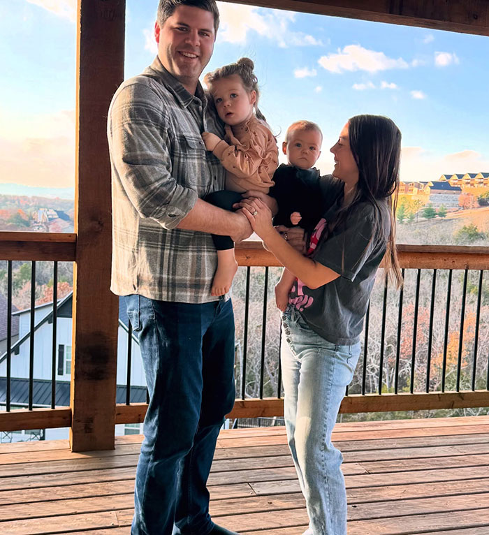 Family on a wooden deck, man holding toddler, woman holding baby, scenic view.