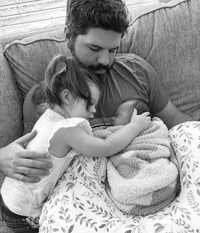 Father holding two young children on a sofa, showing comfort and care.